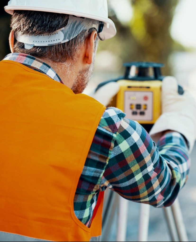Geodesist in orange vest measuring with a total station